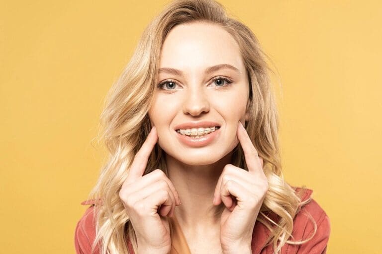smiling blonde woman clear braces looking camera isolated yellow - Clear Braces vs Metal Braces in Sunnyvale, TX