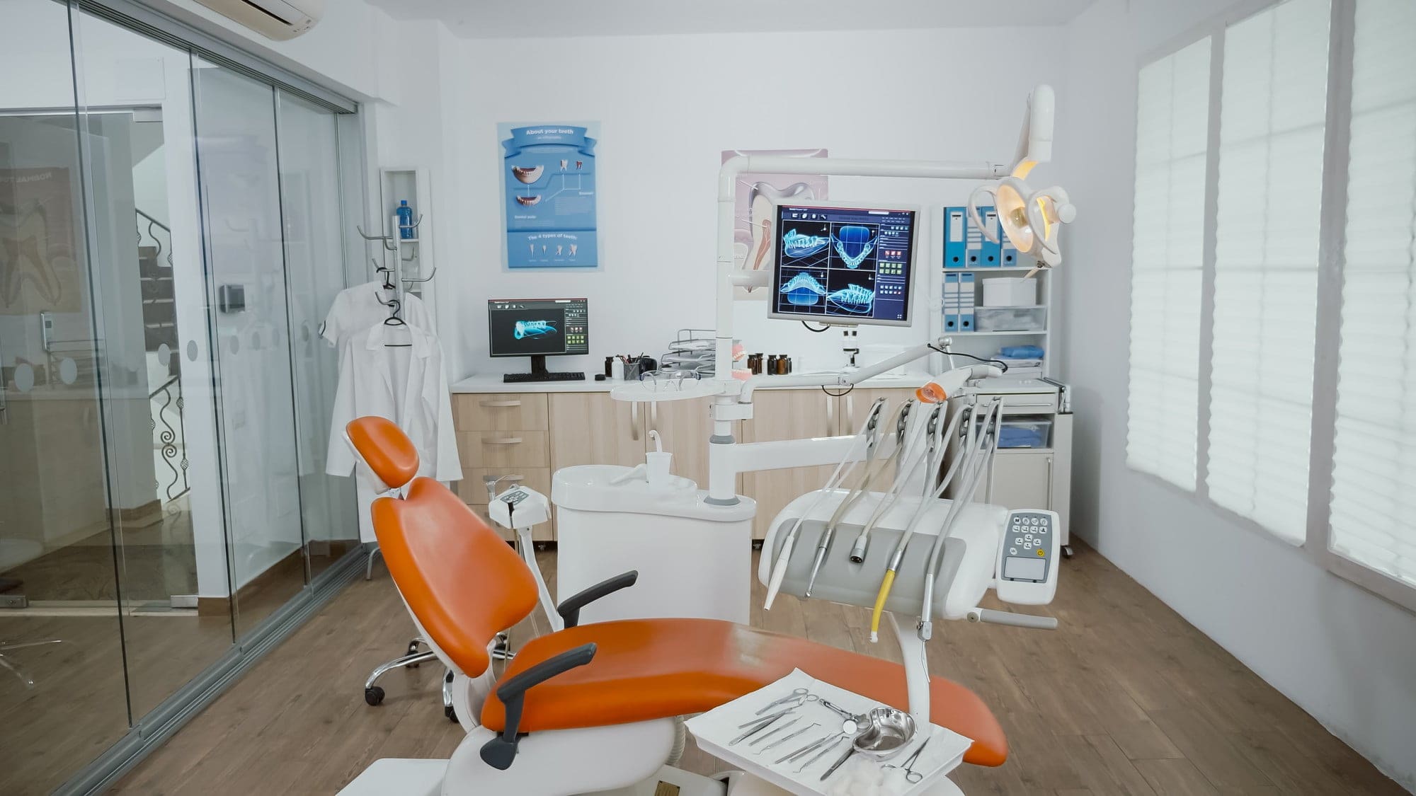 Inside Smile City Orthodontics in Sunnyvale, TX, a modern dental clinic room features an orange dentist chair, dental tools, computer monitors with dental images, and medical equipment in a welcoming space offering a Free Orthodontic Consultation.