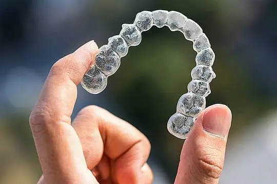 A hand displays a clear Invisalign aligner with a blurred background, showcasing Smile City Orthodontics in Sunnyvale, TX.