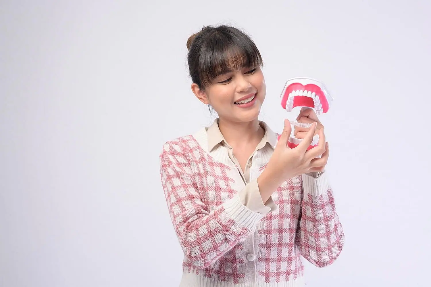 At Smile City Orthodontics in Sunnyvale TX, a woman in a pink plaid sweater examines a model of teeth with Invisalign aligners against a plain white background.