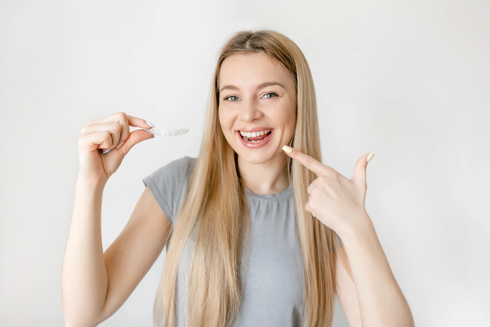 a woman pointing her teeth holding clear aligners - How Long Does Invisalign Take? What the Timeline Really Depends On, Sunnyvale TX
